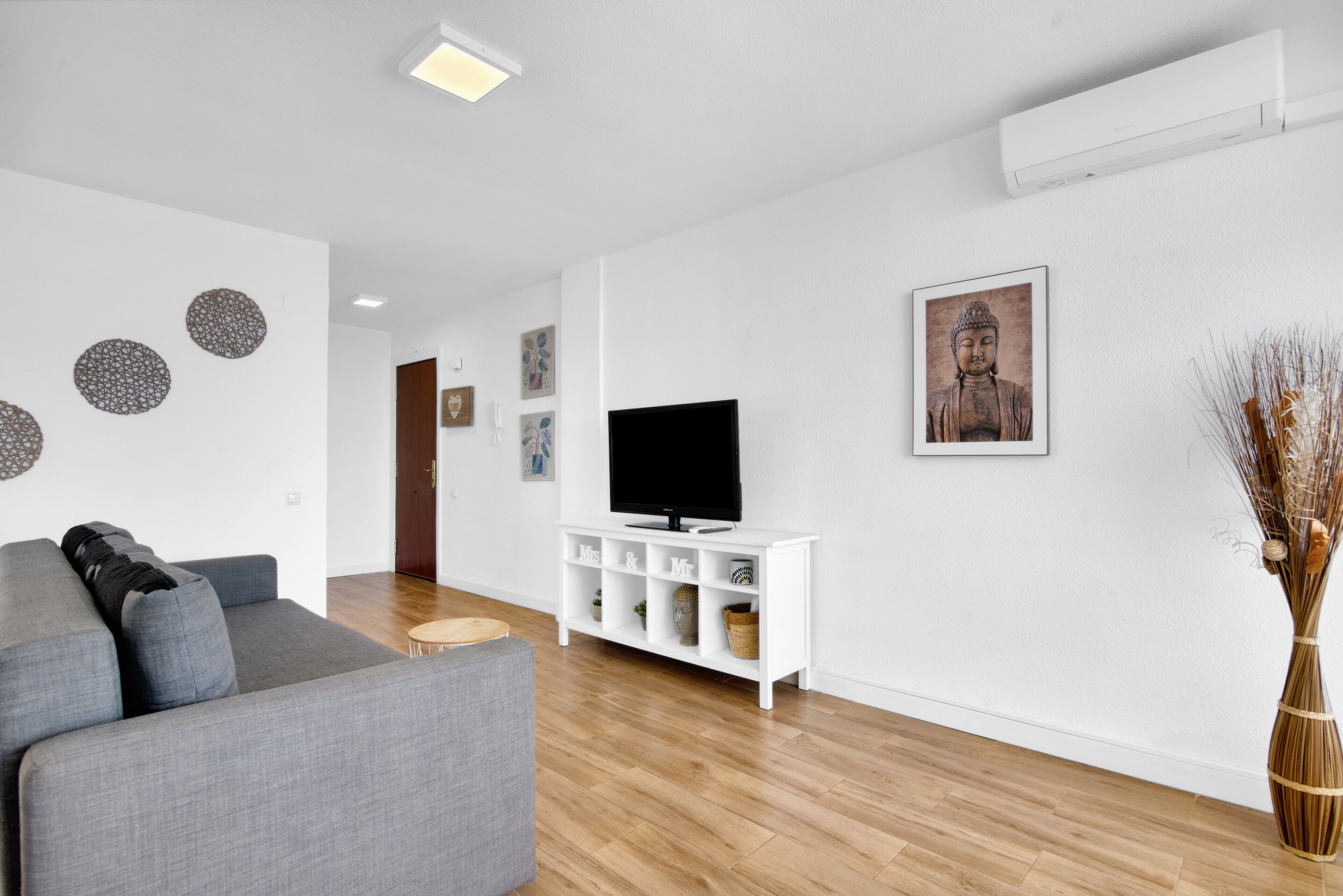 A modern living room with a grey sofa, a white entertainment unit, and a flat-screen TV.