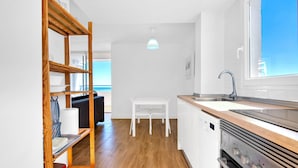 A modern kitchen with wooden shelves, a white table, and a view of the sea. - Apartment 'Playa Puig' with Shared Pool, Wi-Fi and Air Conditioning (El Puig de Santa Maria)