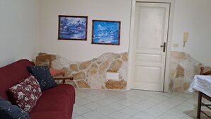 Ein Wohnzimmer mit einem roten Sofa, zwei gerahmten Bildern, einem Holzstuhl, einer Steinwand und einem gefliesten Boden.
