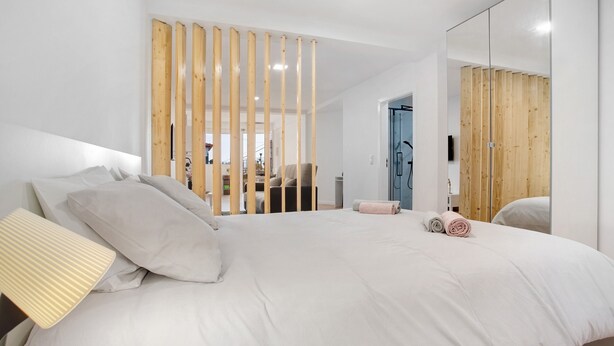 A modern bedroom with a large bed, a wooden partition, a mirror, and a view of the outside. - Studio Apartment 'Babosas Charm' with Mountain View, Wi-Fi and Air Conditioning (Funchal)