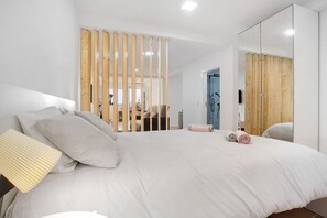 Een moderne slaapkamer met een groot bed, een houten scheidingswand, een spiegel en uitzicht op buiten.