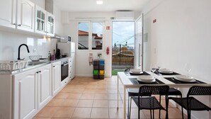 A modern kitchen with white cabinets, a stove, and a dining area with a table set for two. - Studio Apartment 'Babosas Charm' with Mountain View, Wi-Fi and Air Conditioning (Funchal)
