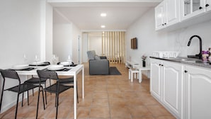 A modern kitchen with white cabinets, a dining area with black chairs, and a grey sofa in the background. - Studio Apartment 'Babosas Charm' with Mountain View, Wi-Fi and Air Conditioning (Funchal)