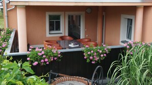 Une terrasse avec une table et des chaises, un petit foyer en briques et des jardinières suspendues.