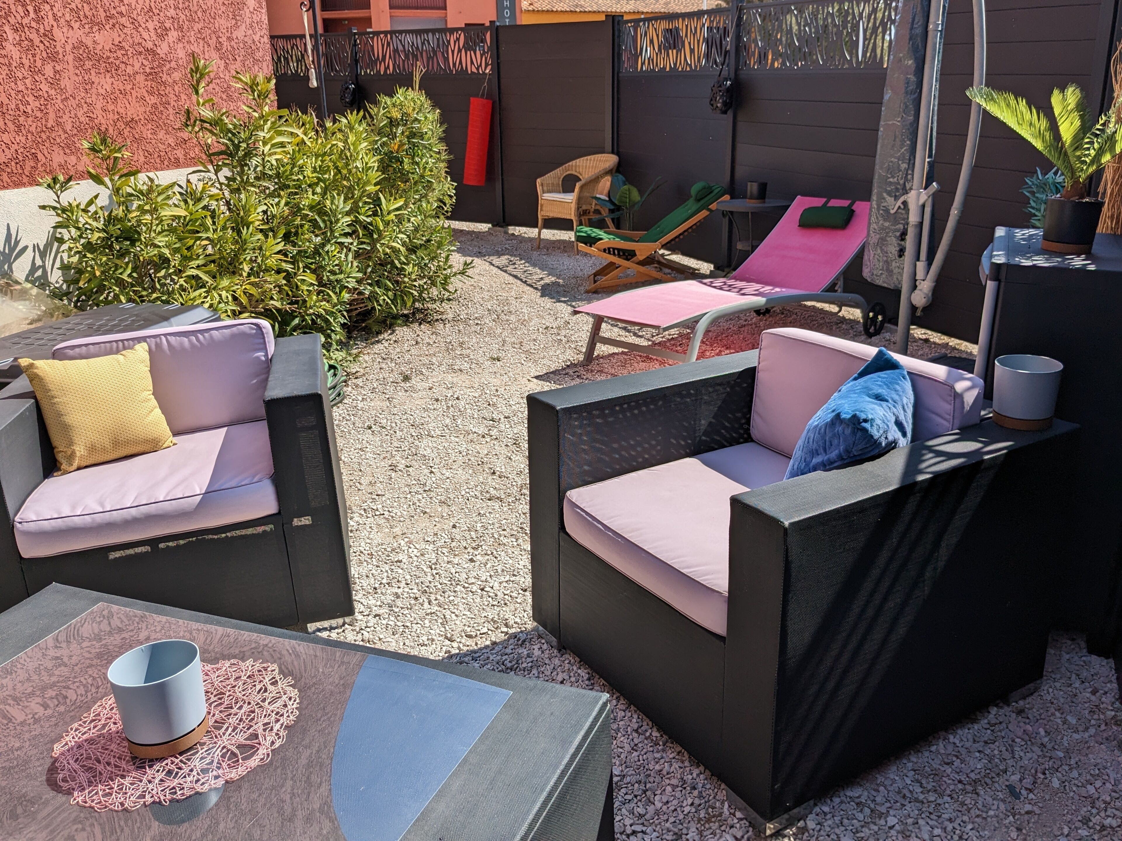 Un’area patio con mobili da esterno, tra cui due divani e un tavolo, circondata da ghiaia e piante.