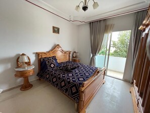 A bedroom with a wooden bed, a nightstand, a lamp, and a view of the outdoors. - Casa Hotel & Hammam Spa (Fernana)
