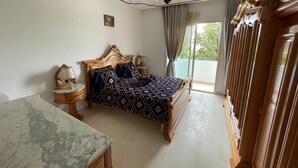 Een slaapkamer met een houten bed, een marmeren nachtkastje, een nachttafel, een kroonluchter en uitzicht op de omgeving door een schuifglazen deur.