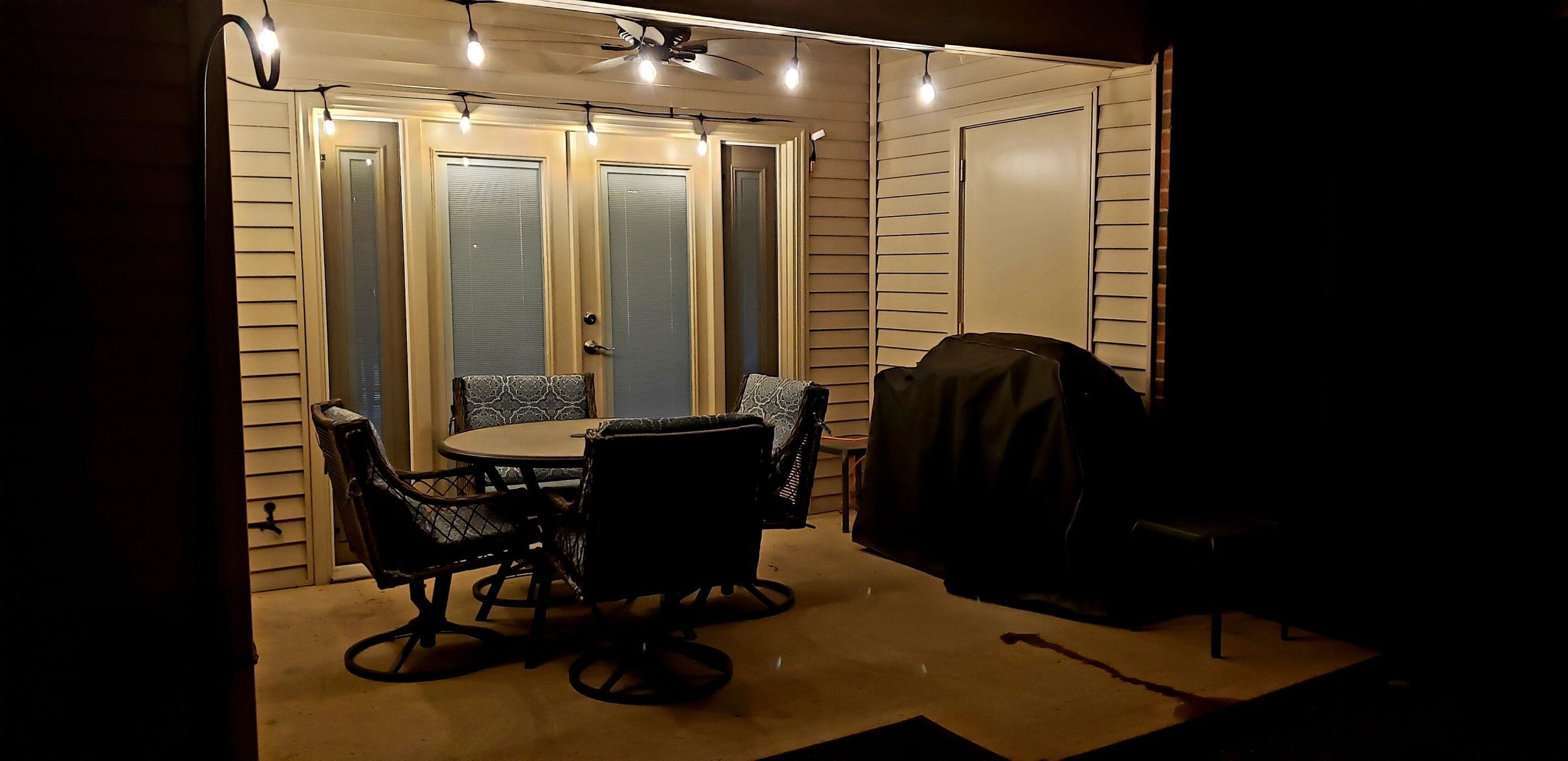 A patio area with a round table and chairs, a grill, and a ceiling fan.