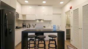 A modern kitchen with white cabinets, a black refrigerator, a central island with stools, and a microwave.