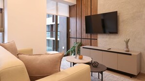 A modern living room with a sofa, a small round table, a cabinet, and a flat-screen TV mounted on the wall.