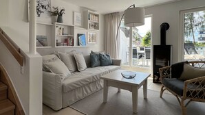 Un salon moderne avec un canapé, une table basse et un fauteuil en osier. On y trouve une bibliothèque remplie de livres et un téléviseur.