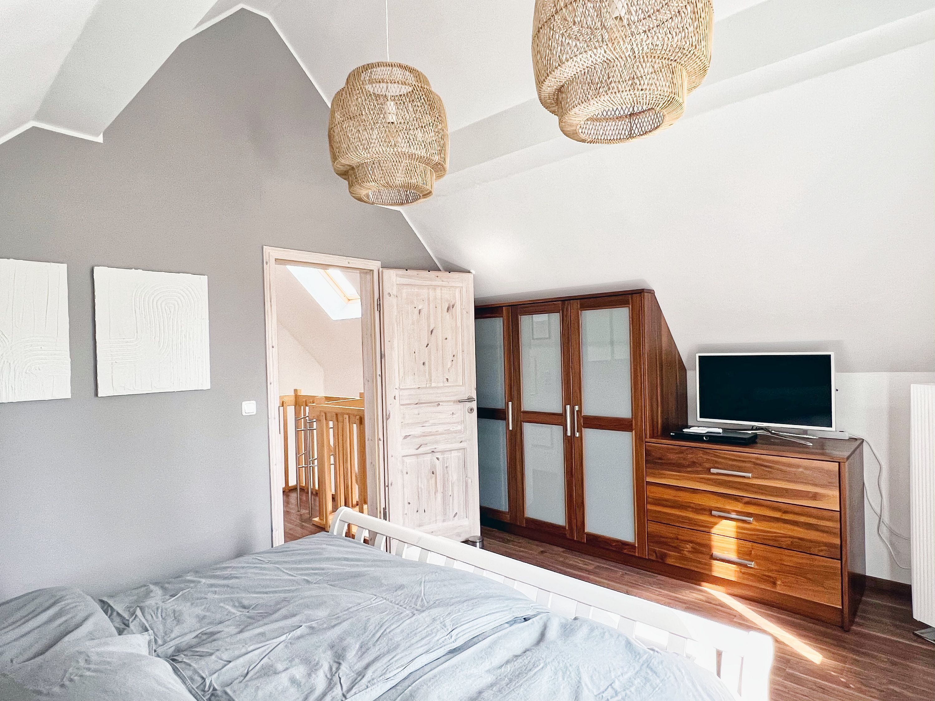 Een slaapkamer met een bed, een houten garderobe, een televisie en twee wandlampen.