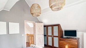 Une chambre à coucher comprenant un lit, une armoire en bois, un téléviseur et deux lampes fixées au mur.