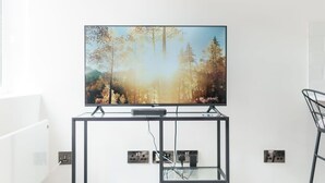 Una televisione a schermo piatto montata su un supporto in metallo nero con ripiano in vetro, davanti a una parete bianca.