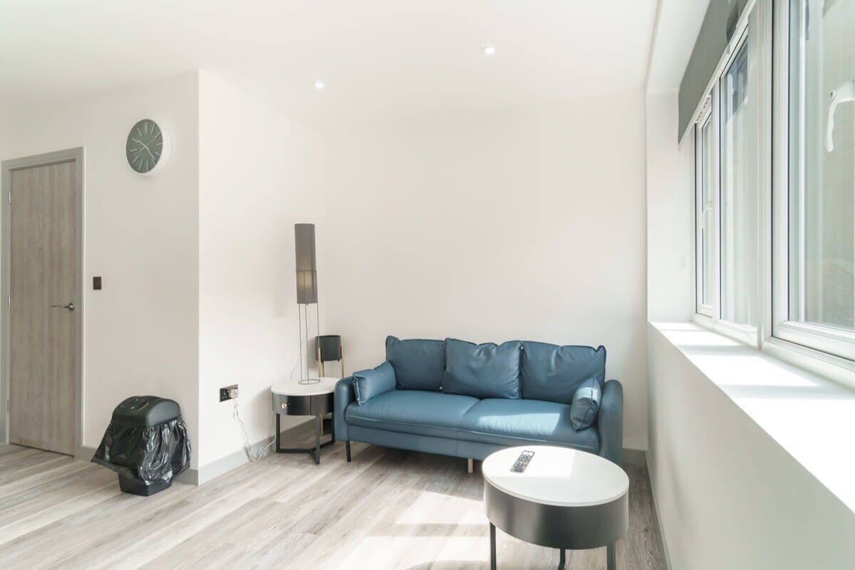 A modern living room with a blue leather sofa, a small round table, a lamp, and a large window.