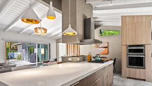 Een moderne keuken met een groot kookeiland, inbouwovens en hangende lampen.