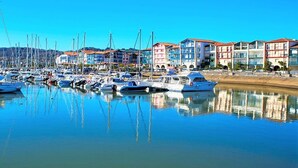 Un port de plaisance avec des bateaux amarrés, des bâtiments aux toits rouges et un ciel bleu clair.
