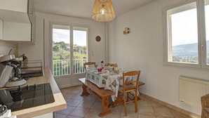 Una cocina con estufa, una mesa de comedor con sillas, una lámpara colgante y vistas a través de una ventana.