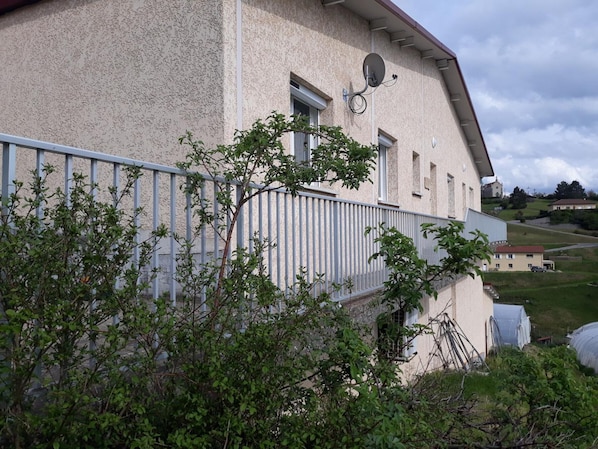 A building with a balcony, a satellite dish, and a view of a church and houses in the background. - Charming country cottage near the Pilat (Saint-Romain-en-Jarez)