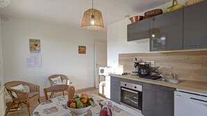 Una cocina compacta con electrodomésticos modernos, un comedor con sillas de mimbre y una lámpara colgante.