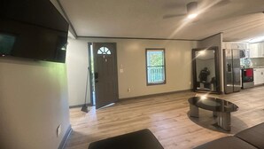 Een moderne woonkamer met een flatscreen televisie, een eettafel en een keuken met roestvrijstalen apparatuur.