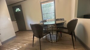 Een eetgedeelte met een ronde tafel, vier stoelen, een raam met zonwering en een deur.