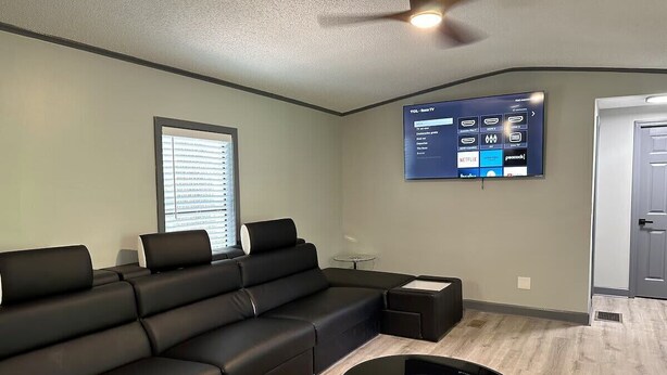 Een moderne woonkamer met een hoekbank, een salontafel, een flatscreen-tv aan de muur en een deur op de achtergrond.