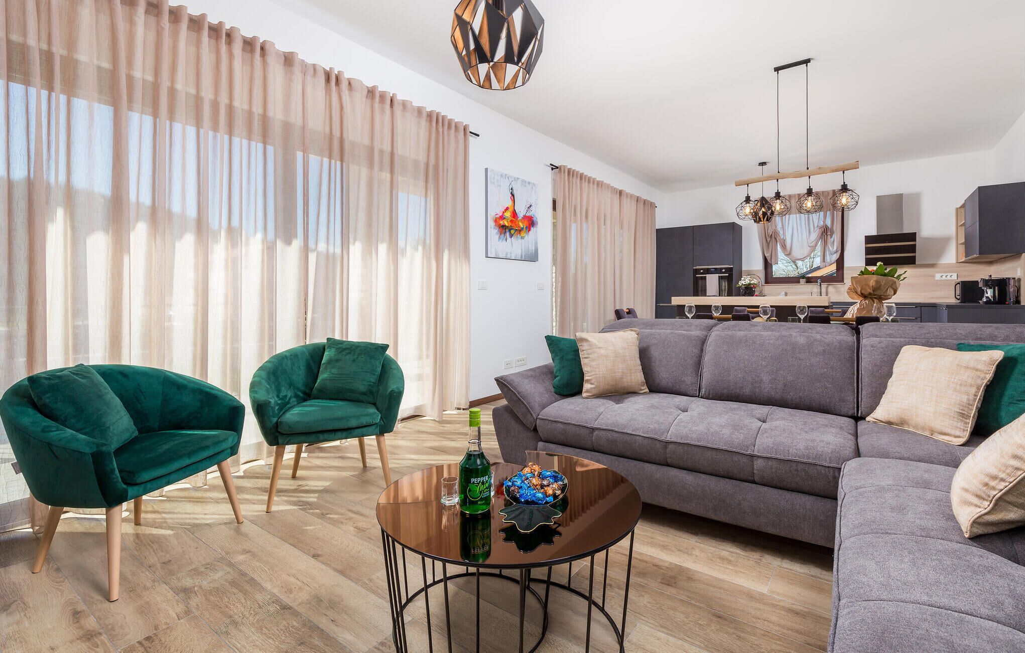 A modern living room with a grey sofa, two green armchairs, and a coffee table with a bottle and decorative bowl.