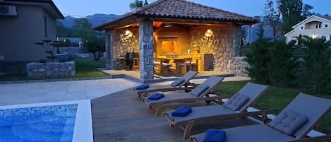 A stone patio with lounge chairs and a pool.