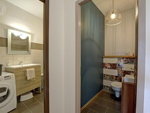 A modern bathroom with a washing machine, a sink with a mirror, a toilet, and a shower area.