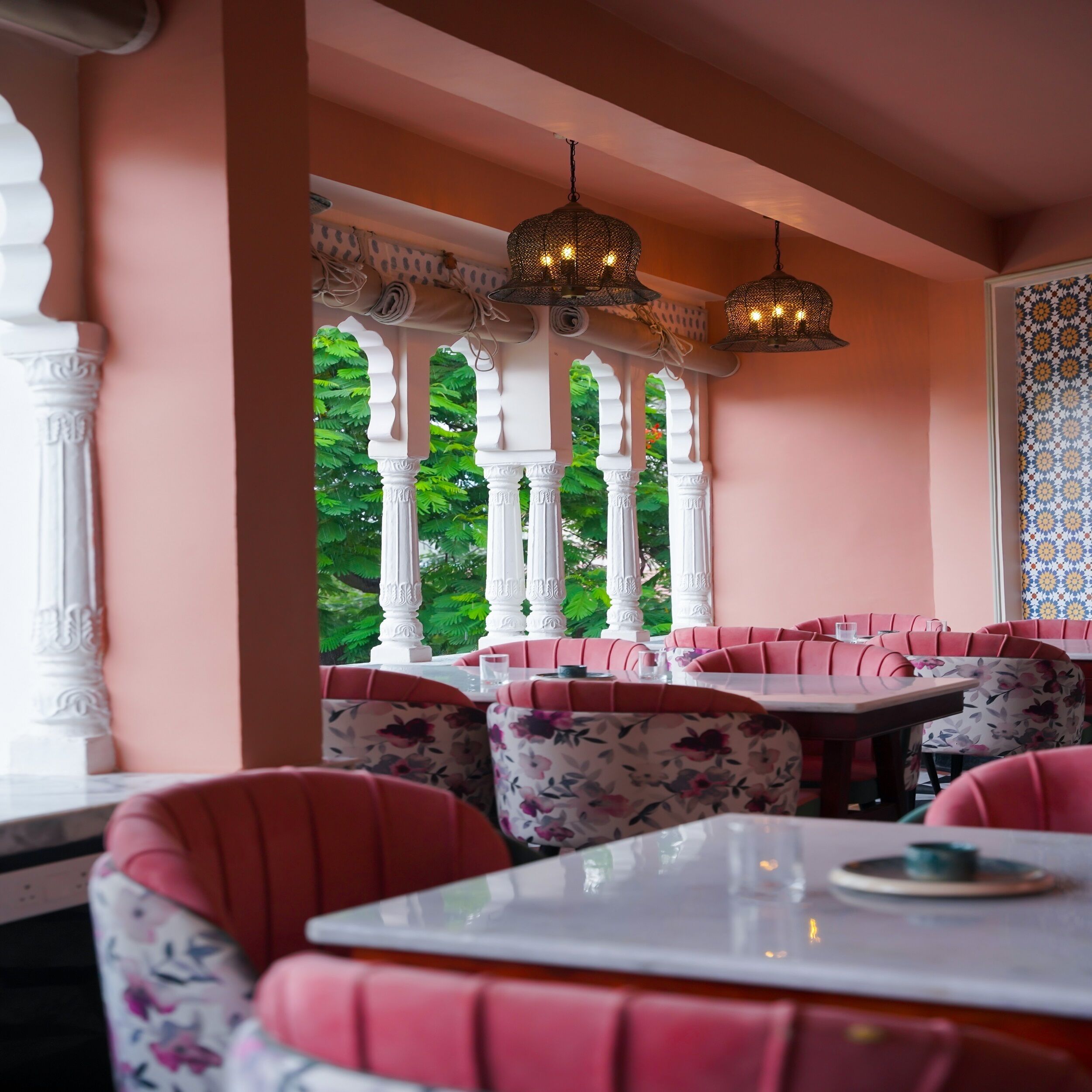 Un ristorante con sedute in stile rosa e colonne bianche, che offre vista su spazi verdi.