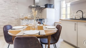 A modern kitchen with a dining area, featuring a wooden table set for four, a built-in oven, and a microwave. - Charming stone house with courtyard and terrace in Créances (Créances)