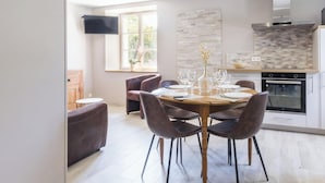 A modern kitchen with a dining area, a flat-screen TV mounted on the wall, and a window with a view of greenery. - Charming stone house with courtyard and terrace in Créances (Créances)