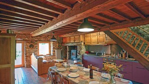 A rustic kitchen with wooden beams, a stone wall, and a dining area with a table set for four.