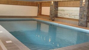 Une piscine intérieure agrémentée de piliers en pierre et de lambris en bois.