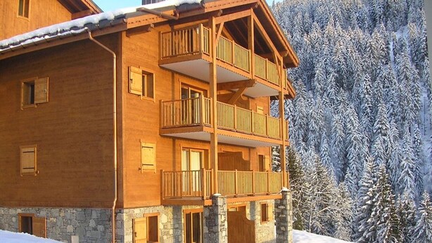 Un chalet en bois à plusieurs étages, doté de balcons, qui se dresse sur fond de montagnes enneigées.
