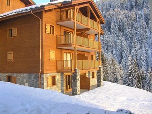 Una cabaña de madera de varios pisos con balcones, con una imponente montaña nevada de fondo.