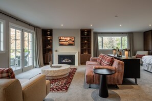 Cozy living room with a fireplace, sofa, and coffee table, featuring a large window and shelves.