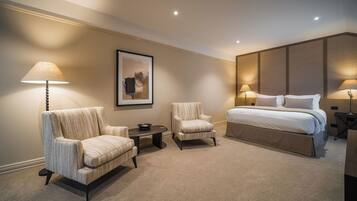 A hotel room with a large bed, two armchairs, a small table, and a framed picture on the wall.