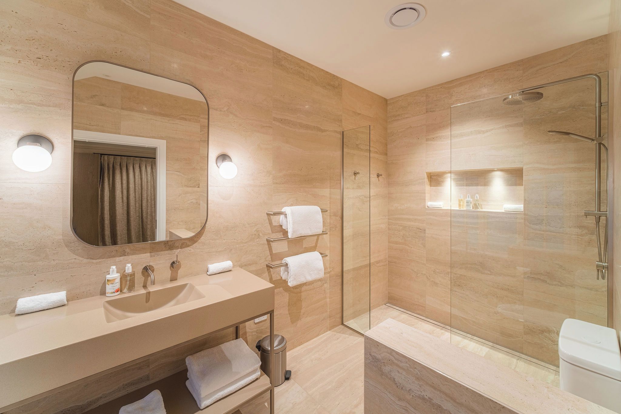A modern bathroom with a large mirror, a sink, a glass-enclosed shower, and a vanity with a towel rack.