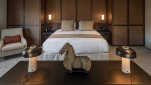 Ein modernes Schlafzimmer mit einem großen Bett, zwei Nachttischlampen, einer dekorativen Skulptur eines Pferdes und einem Sessel.