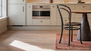 Eine moderne Küche mit hellen Schränken, einem eingebauten Backofen und einem Essbereich mit Tisch und Stühlen.