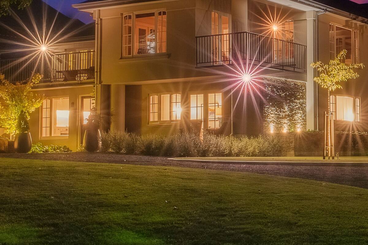 A two-story house with a balcony on the second floor, a well-maintained lawn, and a clear night sky.
