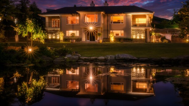 Ein großes, zweistöckiges Haus mit einer gut beleuchteten Veranda und einem Teich im Vordergrund.