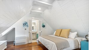 A bedroom with a sloped ceiling, wooden flooring, a bed with white and beige bedding, a blue side table, and a fan. - 'Garden Cottage' at The Broad Street Residences (Charleston)