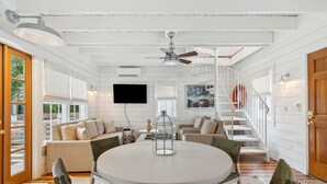 A room with a round table, chairs, a ceiling fan, a TV, and a staircase. - 'Garden Cottage' at The Broad Street Residences (Charleston)