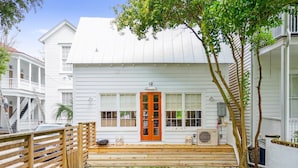 A white two-story house with a wooden deck, a front door, and a small porch. - 'Garden Cottage' at The Broad Street Residences (Charleston)