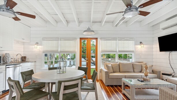 A spacious living area with a round dining table, green cushioned chairs, a beige sofa, and a glass coffee table. - 'Garden Cottage' at The Broad Street Residences (Charleston)