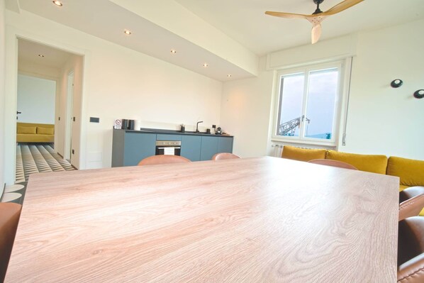 Une pièce spacieuse avec une grande table à manger en bois, un coin cuisine doté d’un plan de travail bleu et un canapé jaune.