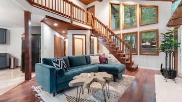 A spacious living area with a wooden staircase, a sectional sofa, and a large window providing natural light.
